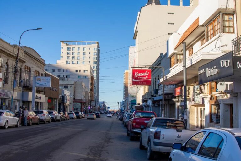Calle comercial en Comodoro Rivadavia con cartel de 'Se Vende' en un local