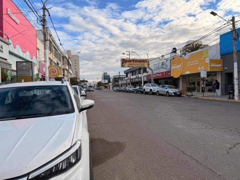 Calle céntrica de Puerto Madryn con autos estacionados y comercios de fondo