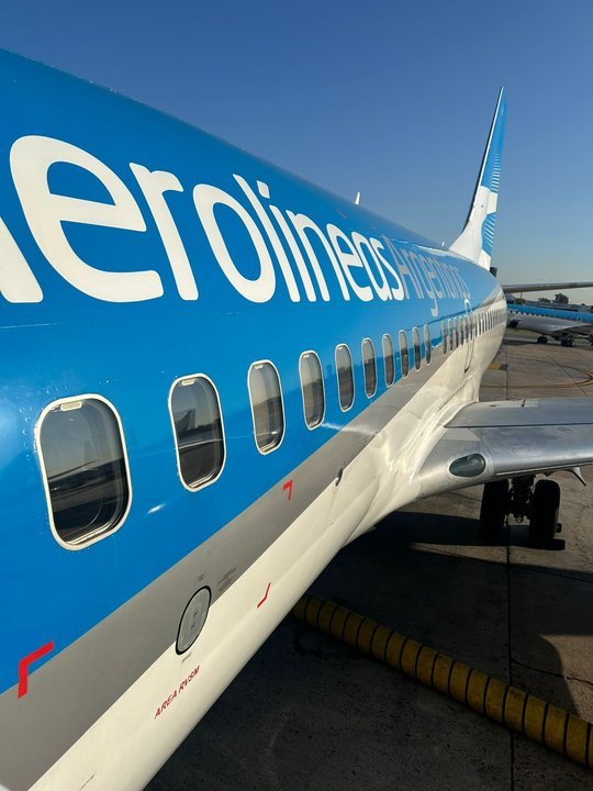 Avión de Aerolíneas Argentinas en pista de aterrizaje con paisaje de montaña de fondo