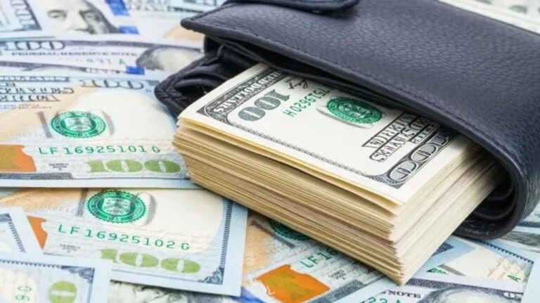 Billetes de dólar estadounidense y billetes de peso argentino sobre una mesa, con una calculadora y una laptop