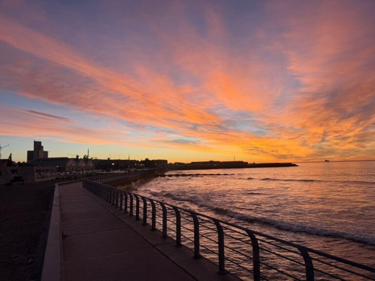 Vista de la costa de Comodoro Rivadavia con cielo nublado y banderas ondeando por el viento